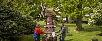 Gut Sassenscheid Zwei Menschen bemalen gemeinsam eine Windmühle in einem Garten.